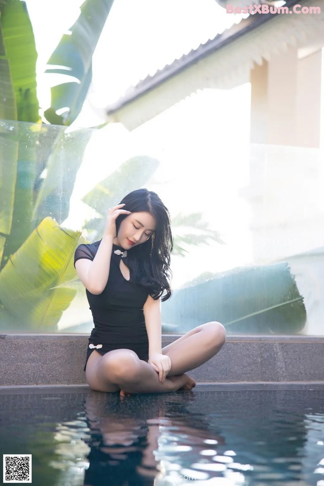 A woman in a black bathing suit sitting on the edge of a pool.