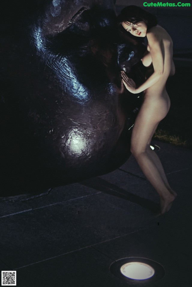 A naked woman standing next to a giant gorilla.