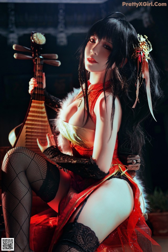 A woman in a red dress sitting on a chair holding a musical instrument.