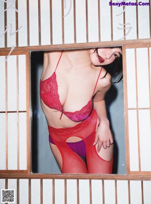 A woman in a red lingerie is looking out of a window.