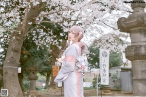 A woman in a kimono standing in front of a stone pillar.