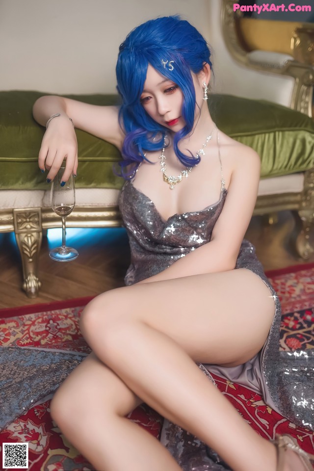 A woman with blue hair sitting on a couch holding a glass of wine.