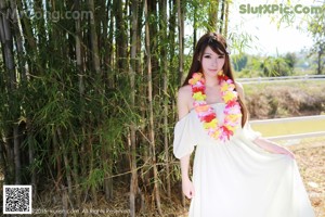 A woman in a white dress standing next to a tree.