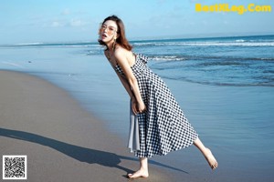 A woman walking on the beach talking on a cell phone.