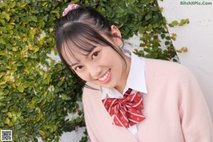 A young woman wearing a pink cardigan and a red bow tie.