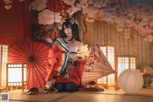 A woman in a kimono sitting on the floor with an umbrella.