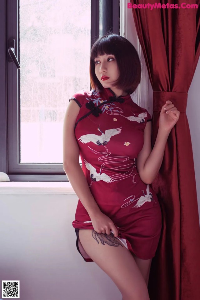 A woman in a red dress leaning against a window.