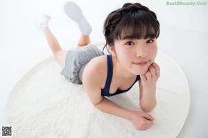A young woman sitting on a white rug with her legs crossed.
