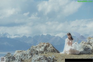 A woman in a white dress sitting on a rock holding a mirror.