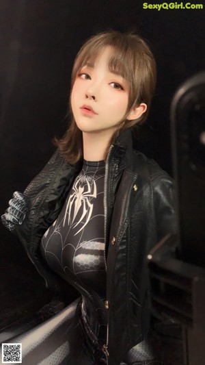 A woman in a black leather jacket sitting on a pink chair.
