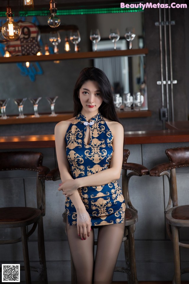 A woman in a blue and gold dress sitting at a bar.