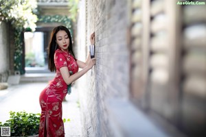 A woman in a red dress leaning against a column.